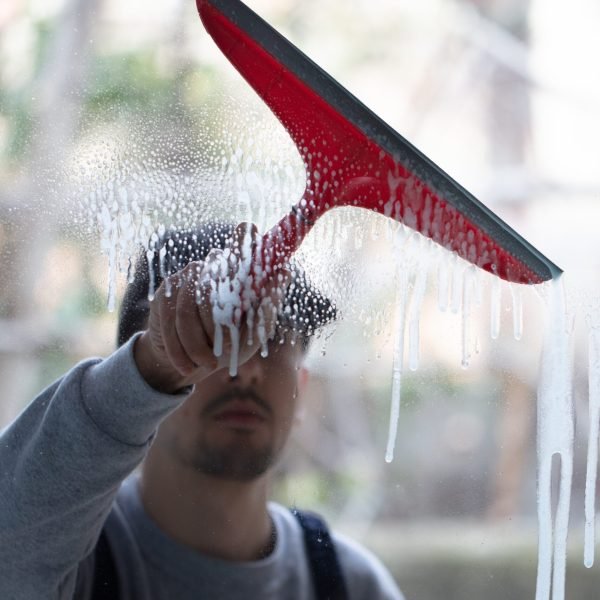 A closeup of a person cleaning windows with a red squeegee under the lights with a blurry background