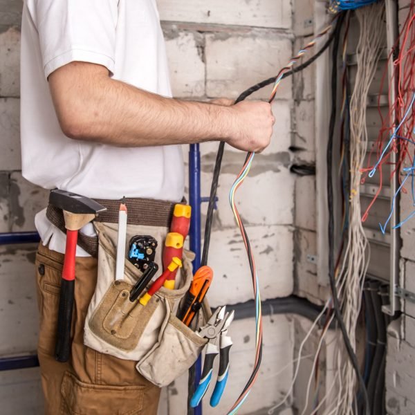 Electrician working near the Board with wires. Installation and connection of electrics. Professional with tools in hand.